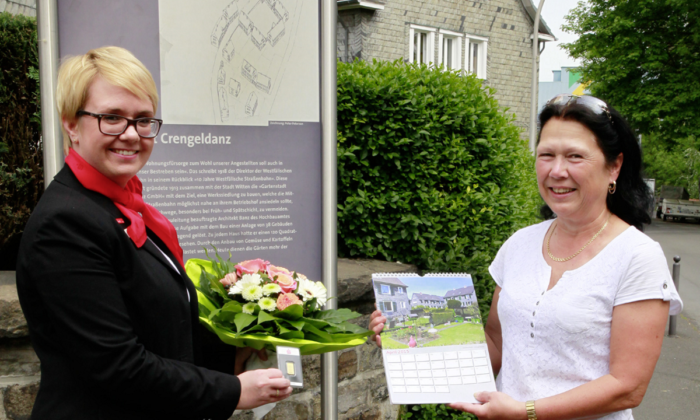 Cornelia Rüsing (rechts) ist die Gewinnerin des April-Rätsels im Sparkassenkalender 2015. Vor dem Eingang zur „Gartenstadt Crengeldanz“ an der unteren Schottstraße gratulierte Stefanie Matuschek, Leiterin der benachbarten Sparkassengeschäftsstelle, mit einem Blumenstrauß und übergab einen 5-Gramm-Goldbarren.